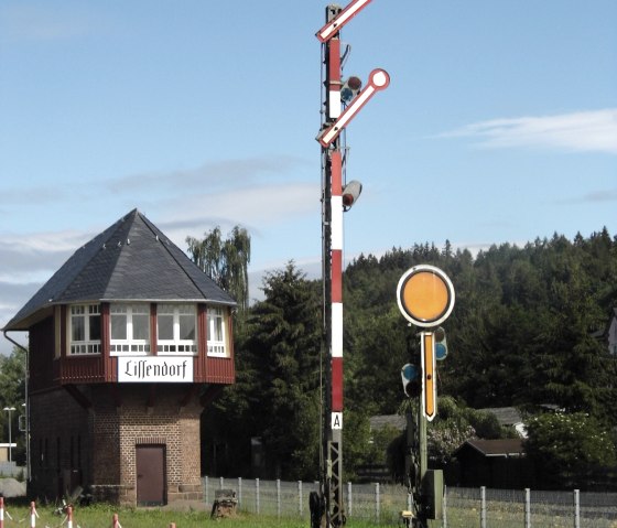 Ancien poste d'aiguillage 'Lissendorf' et signal ferroviaire mécanique sur fond de ciel bleu, entouré d'un paysage verdoyant., © Herr Schun Ancien poste d'aiguillage 'Lissendorf' et signal ferroviaire mécanique sur fond de ciel bleu, entouré d'un paysage verdoyant., © Herr Schun