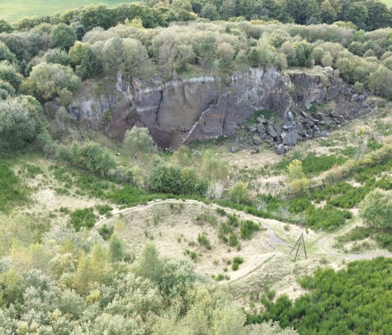 Vue aérienne de la région boisée avec la paroi rocheuse du Steffelberg et des prairies vertes. Un sentier serpente à travers le paysage., © Touristik GmbH Gerolsteiner Land, Sarah Wiesen Vue aérienne de la région boisée avec la paroi rocheuse du Steffelberg et des prairies vertes. Un sentier serpente à travers le paysage., © Touristik GmbH Gerolsteiner Land, Sarah Wiesen