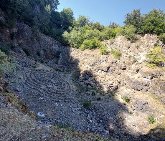 Labyrinthe de pierres dans la fosse rocheuse du volcan Arensberg, entouré d'arbres et d'un ciel bleu., © Touristik GmbH Gerolsteiner Land Labyrinthe de pierres dans la fosse rocheuse du volcan Arensberg, entouré d'arbres et d'un ciel bleu., © Touristik GmbH Gerolsteiner Land