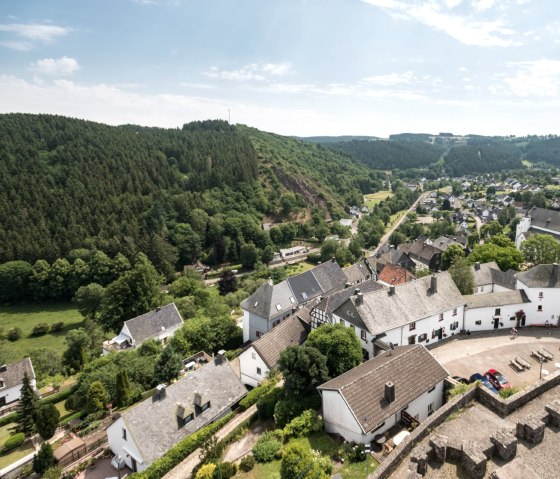 Panoramablick vom Burgturm Reifferscheid auf ein malerisches Dorf mit Kirche, umgeben von grünen Hügeln und Wäldern unter blauem Himmel., © Eifel Tourismus GmbH/D. Ketz Panoramablick vom Burgturm Reifferscheid auf ein malerisches Dorf mit Kirche, umgeben von grünen Hügeln und Wäldern unter blauem Himmel., © Eifel Tourismus GmbH/D. Ketz