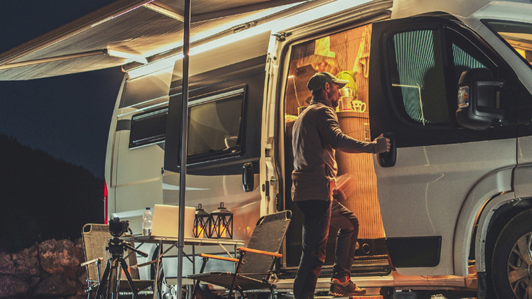 <p>Eine person steigt in sein Wohnmobil ein. Draußen ist es dunkel, das Licht im Innenraum ist an. Es ist ein Pavillon an der Seite des Wohnmobils gespannt.</p>