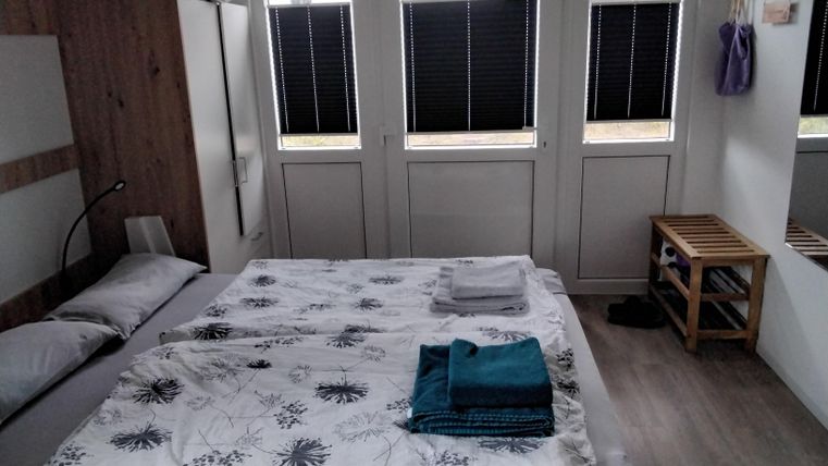 Ein einfaches Schlafzimmer mit einem Doppelbett, frischen Handtüchern und großen Fenstern. Die Wände sind hell und das Zimmer wirkt gemütlich und einladend.