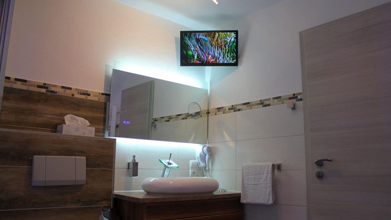 Ein modernes Badezimmer mit einem eleganten Waschbecken und einem Fernseher an der Wand. Die helle Beleuchtung sorgt für eine freundliche Atmosphäre.