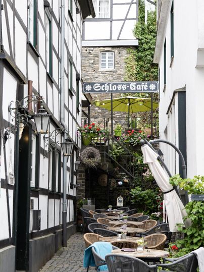 A picturesque alley with a cozy café. Tables are set up outside, surrounded by historic buildings and plants.