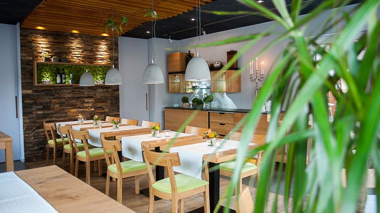 A modern restaurant with bright tables and chairs. The walls are decorated with wood and plants, and there are stylish lamps.
