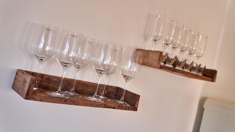 Two wooden shelves with glasses are against the wall. The glasses are upright and neatly arranged.