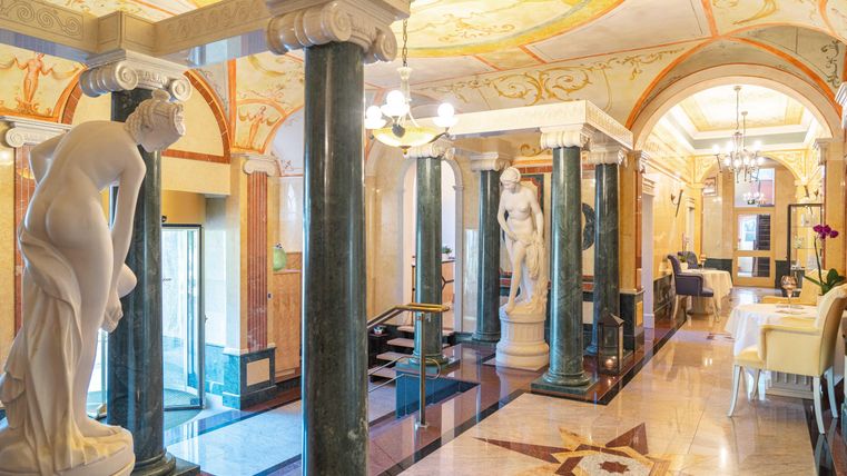 Een elegante entree met zuilen en sculpturen. De wanden zijn kunstzinnig versierd en de vloer heeft een opvallend patroon.