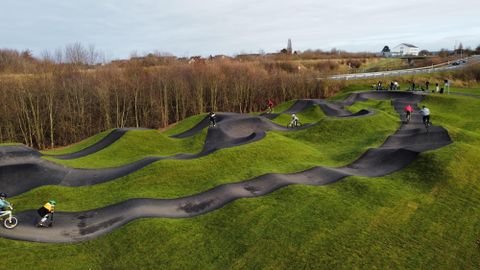 Ein moderner Pumptrack in einer grünen Landschaft. Radfahrer nutzen die Wellen und Kurven für sportliche Aktivitäten.