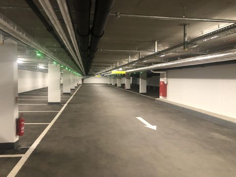 An empty parking lot with several parking spaces and a ceiling with pipes. The lighting is modern, and there are green and yellow light signals.