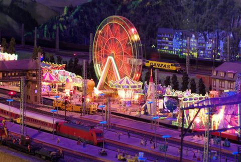 Een levendig advertenties-carousel met een reuzenrad en kleurrijke lichten. Op de achtergrond zijn treinen en een gedetailleerd stadslandschap te zien.