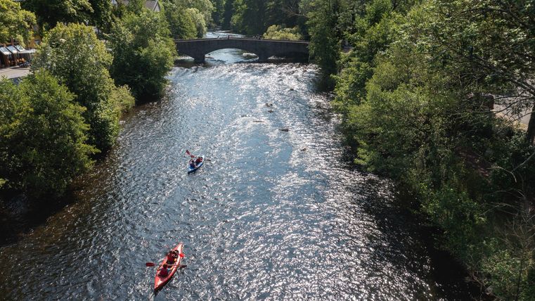 Ein schöner Fluss fließt durch eine grüne Landschaft. Zwei Kajakfahrer paddeln entspannt auf dem Wasser.