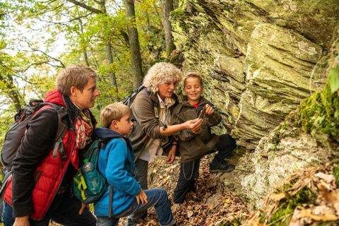 Eine Gruppe von zwei Erwachsenen und zwei Kindern erkundet die Natur. Sie schauen interessiert auf einen Felsen im Herbstwald.