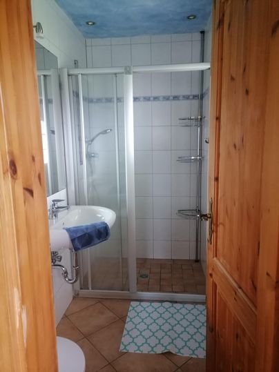 Een heldere badkamer met een douche, een wastafel en een tegelvloer. De muren zijn betegeld, en er is een houten deur.