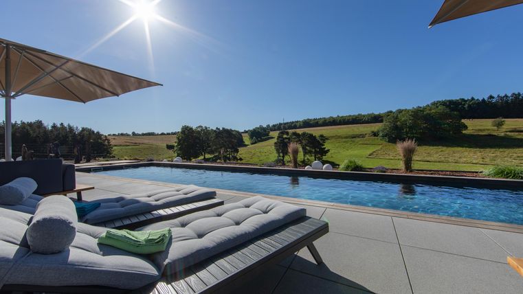 Een prachtig zwembad met ligstoelen en parasols. Op de achtergrond strekt zich een groene landschap uit onder een helderblauwe lucht.