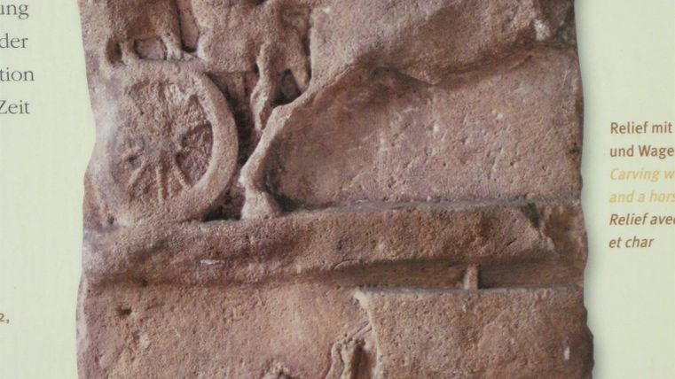 Roman relief shows a figure on a chariot with a horse and another figure holding a sail. Background text partially visible.