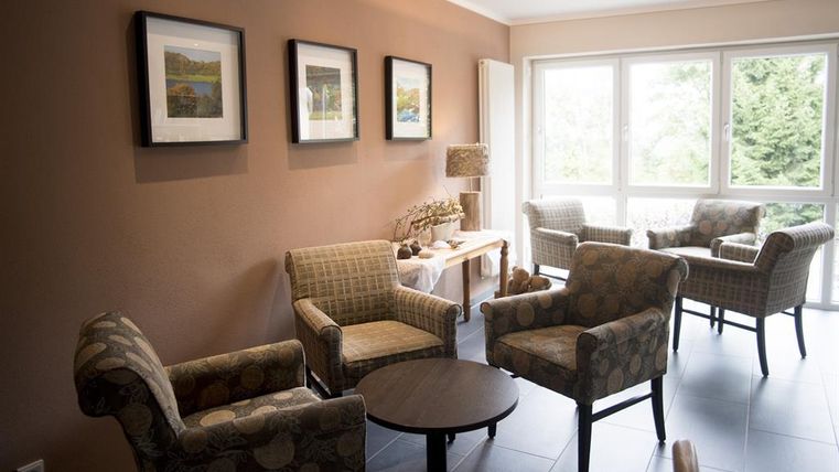 Een gezellige zithoek met vier comfortabele stoelen en een kleine tafel. Aan de muur hangen ingelijste foto's, terwijl grote ramen voor veel daglicht zorgen.