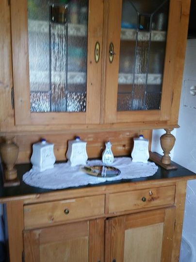 Ein traditioneller Holzschrank mit Glasfronten und zwei unteren Schubladen. Darauf stehen dekorative weiße Behälter und eine Tischdecke.