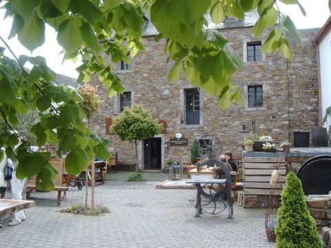 Binnenplaats van een historische molen met stenen muren, tafels en planten. Mensen zitten aan tafels, omringd door groene bladeren en rustieke decoraties.
