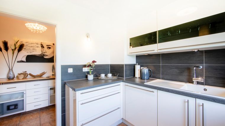 Eine moderne Küche mit hellen Schränken und einer klaren Arbeitsfläche. Im Hintergrund ist eine stilvolle Beleuchtung und Dekoration sichtbar.