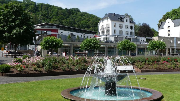 Een mooie fontein in een goed onderhouden park. Op de achtergrond zijn gebouwen en groene bomen te zien.