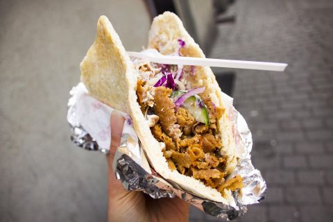 Een döner in één hand gehouden, gevuld met vlees, sla en saus, in aluminiumfolie gewikkeld.
