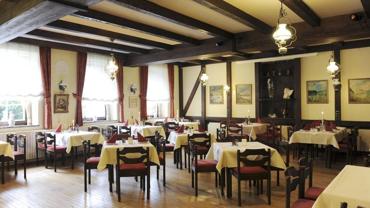 Ein gemütliches Restaurant mit Tischen und Stühlen. Die Holzdecke und die Wände schaffen eine einladende Atmosphäre.