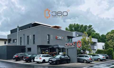 Een modern gebouw met het opschrift "360" staat op de voorgrond. Verschillende auto's parkeren voor het gebouw onder een bewolkte hemel.