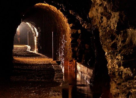 Een ondergrondse tunnel met een ronde muur en stenen wanden. Zwak licht en water staan op de grond.