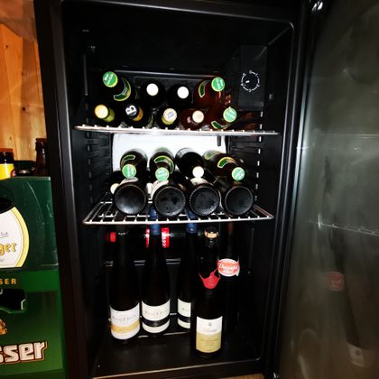 Een koelkast vol flessen, waaronder bier en verschillende wijnen. De flessen zijn netjes op twee planken gerangschikt.