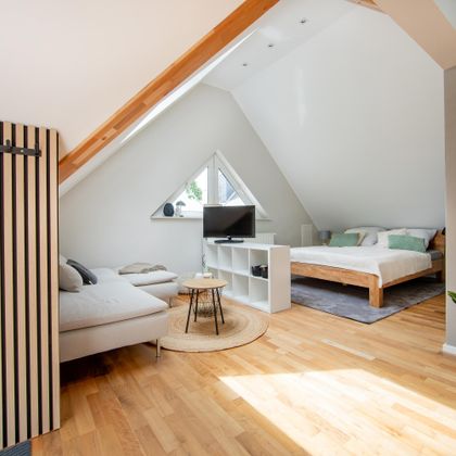 Een moderne kamer met een comfortabele bank en een groot raam. De vloer is van hout en er is een ontspannen sfeer.