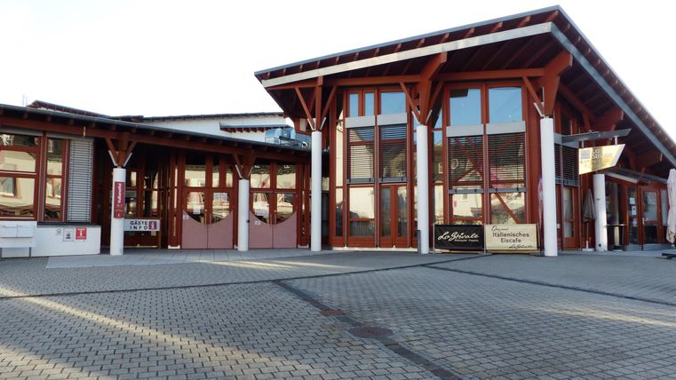 Ein modernes Gebäude mit großen Fenstern und Holzverkleidung. Der Eingangsbereich ist einladend und freundlich gestaltet.