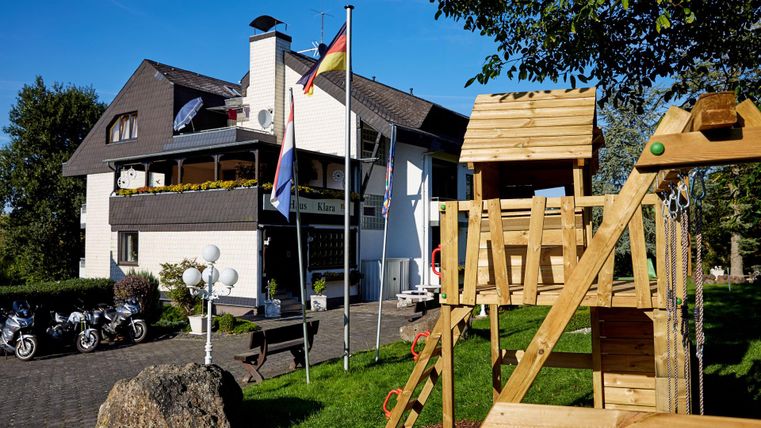 Een modern gebouw met een speeltoestel op de voorgrond. Vlaggen en motorfietsen zijn ook zichtbaar, omringd door groenvoorzieningen.