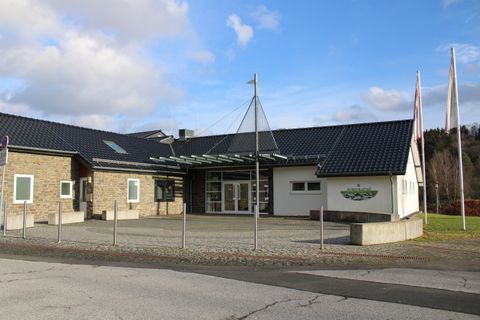 Een modern gebouw met een plat dak en grote ramen. Voor de ingang staan meerdere vlaggen en een verhard gebied.