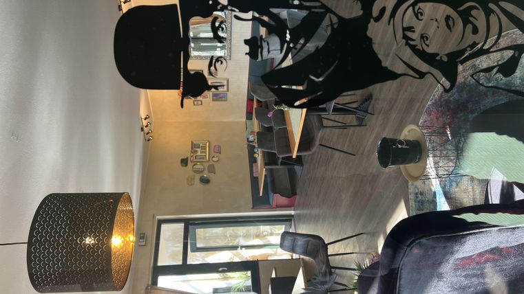 Ein stilvolles Cafe mit modernen Möbeln und einer großen Fensterfront. An der Wand ist eine interessante Silhouette von einer Person mit Zylinder und einem Fernglas zu sehen.