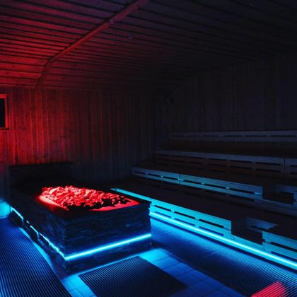 Eine moderne Sauna mit bunten LED-Lichtern und einer rustikalen Holzdekoration. Der Raum ist gemütlich und lädt zur Entspannung ein.