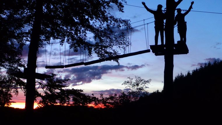 two happy people on a zipline platform at dusk</p>