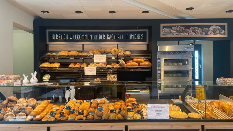 Een uitnodigende bakkerij met een ruime keuze aan versgebakken brood en gebak. Op de toonbank zijn veel producten mooi gepresenteerd, terwijl een welkomstbord de gasten verwelkomt.