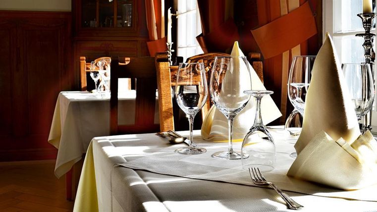 Ein elegant eingedeckter Tisch in einem Restaurant mit Gläsern und Stoffservietten. Sanftes Licht fällt durch die Fenster und schafft eine gemütliche Atmosphäre.