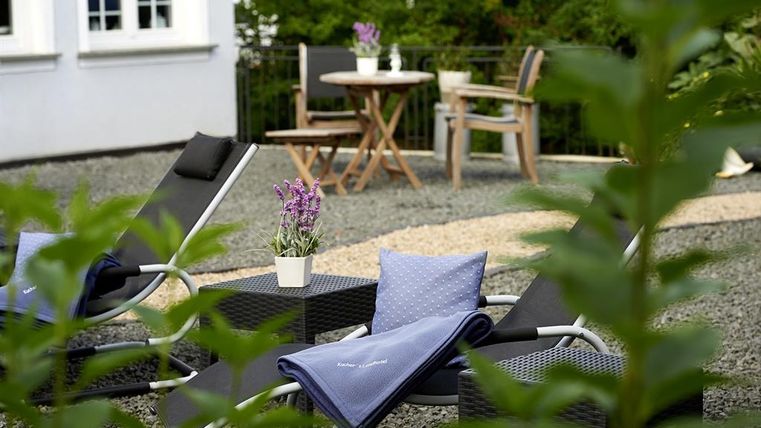 Ein gemütlicher Außenbereich mit Liegen und einem kleinen Tisch. Pflanzen umgeben die Sitzecke und verleihen dem Raum eine entspannte Atmosphäre.