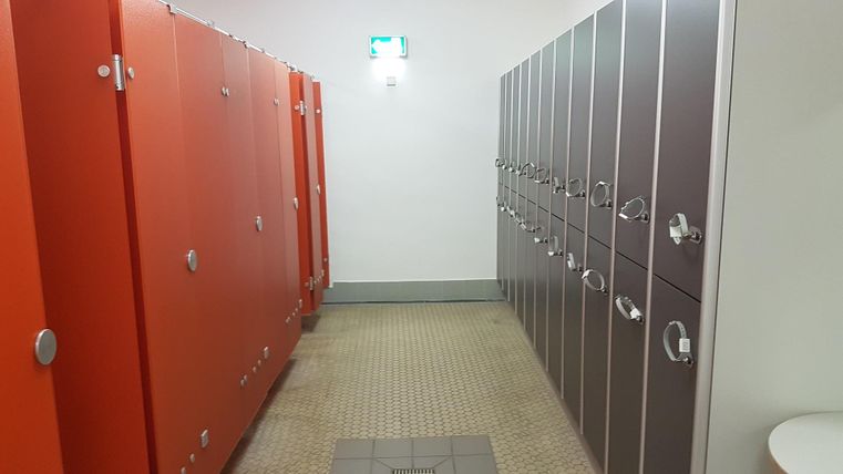 A changing room with orange and gray lockers. The room has bright lighting and a tiled floor.