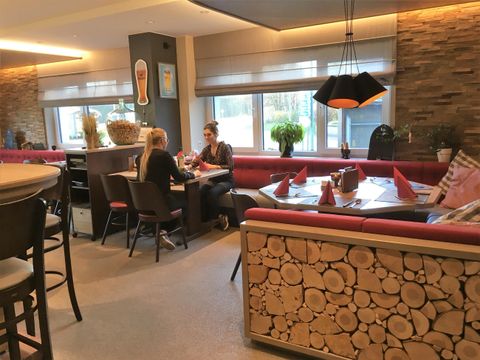 Ein gemütlicher Cafe-Bereich mit roten Sitzbänken und einer Holzdekoration. Zwei Frauen sitzen am Tisch und unterhalten sich.