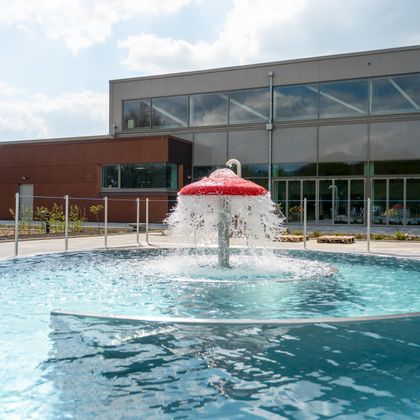 Ein moderner Pool mit einem roten Spritzdach, das Wasser sprüht. Im Hintergrund ist ein Gebäude mit großen Fenstern zu sehen.