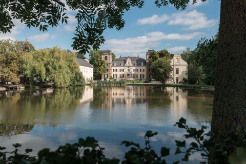 A picturesque landscape with a calm lake and historical buildings in the background. The image conveys a peaceful atmosphere with beautiful weather.