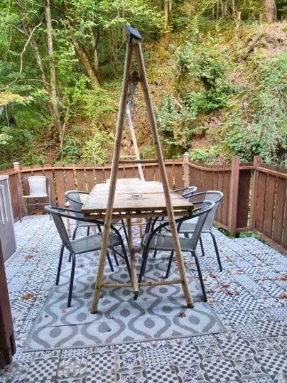 A cozy terrace area with a wooden table and six chairs. Surrounded by trees and a peaceful, green landscape.