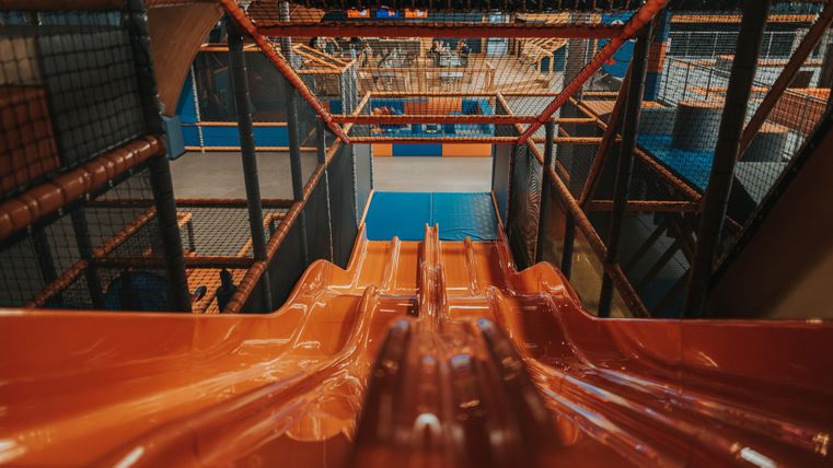 Eine große Rutsche in einem Spielplatz mit vielen Klettergerüsten und Spielbereichen. Der Blick von oben zeigt die farbenfrohe Ausstattung und Aktivitäten für Kinder.