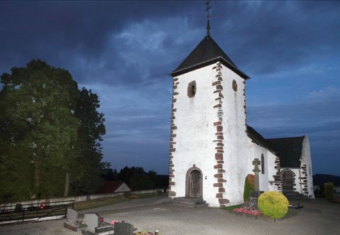 De Wehrkirche Berndorf staat bij schemering in het middelpunt, omringd door bomen en een begraafplaats. De lucht is donkerblauw gekleurd.