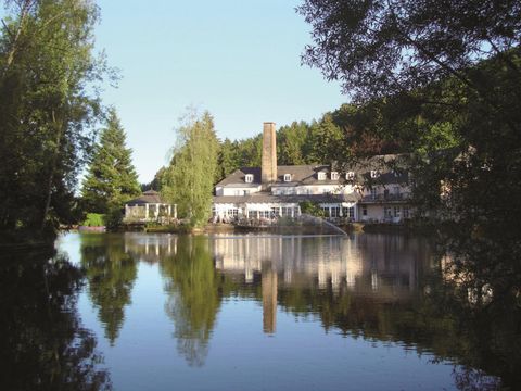 Ein ruhiges Hotel am Ufer eines Sees, umgeben von Bäumen. Die Reflexion des Gebäudes im Wasser schafft eine friedliche Atmosphäre.