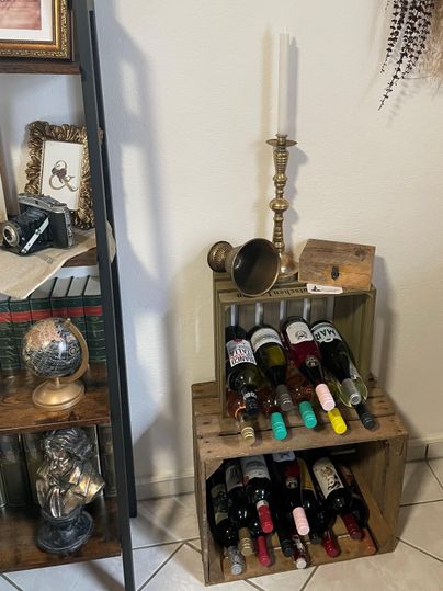 Een stijlvolle wijnrek van hout met meerdere flessen wijn. Bovenop staat een elegante kaars en een messingvoorwerp.