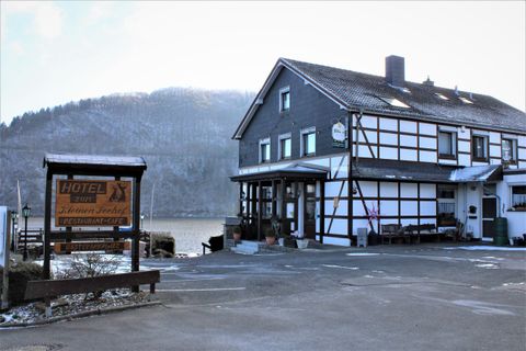 Een schilderachtig herberg met vakwerkarchitectuur aan het water. Op de achtergrond zijn beboste heuvels te zien.