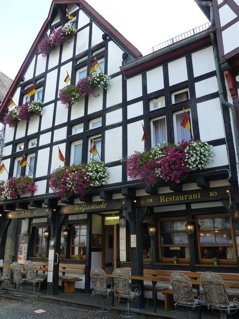 Ein traditionelles Fachwerkhaus mit bunten Blumen und deutschen Flaggen. Das Restaurant lädt mit Außensitzplätzen zum Verweilen ein.